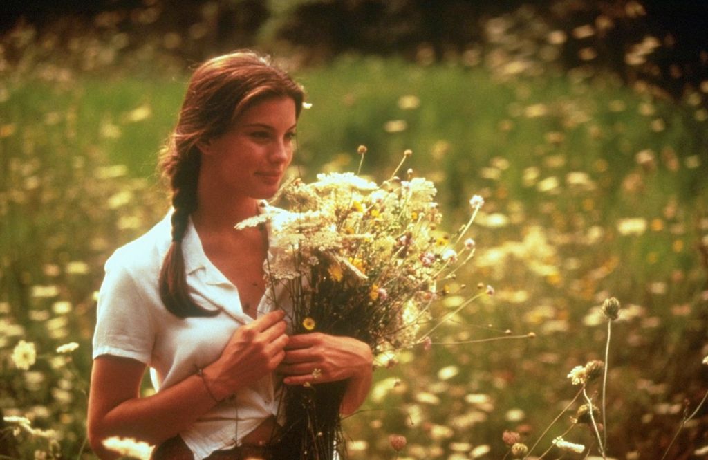 Liv Tyler dans Stealing Beauty, portant un bouquet de fleurs dans un champ.