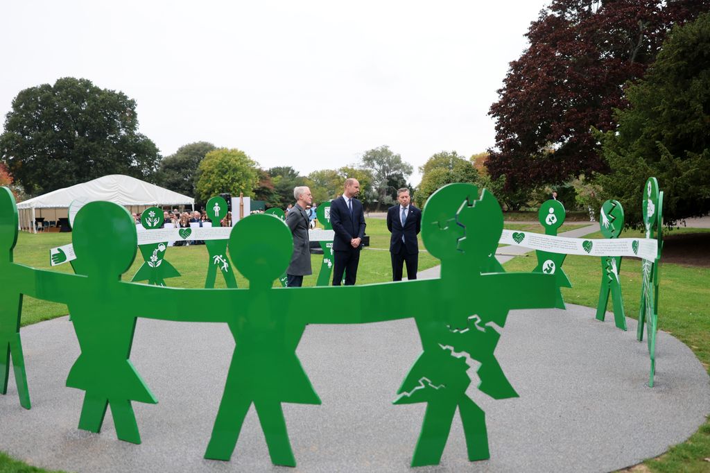 Michael Landy, Prince William, Prince of Wales and Tom Fletcher stand inside green memorial in park