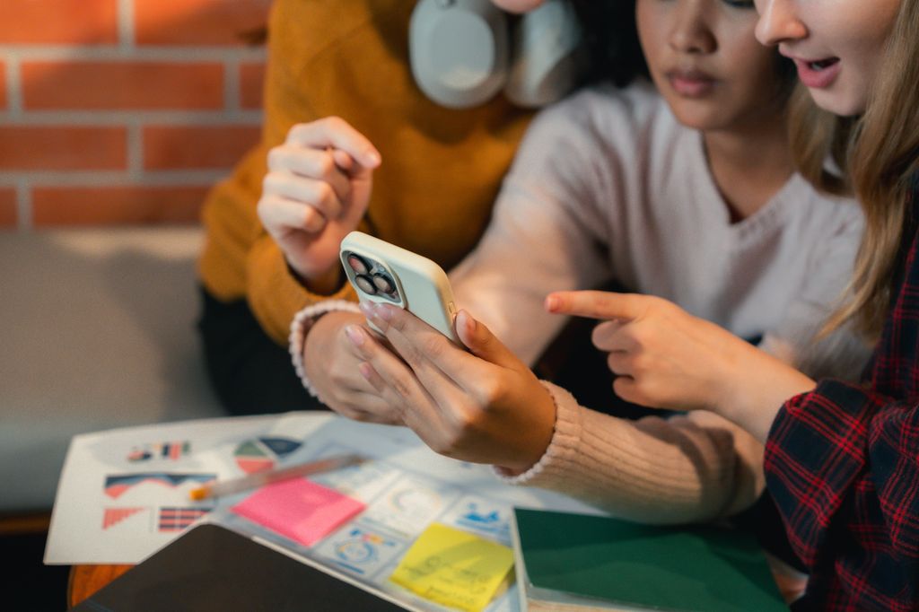 Group of friends gathered around a smartphone, using an app to help with their group project