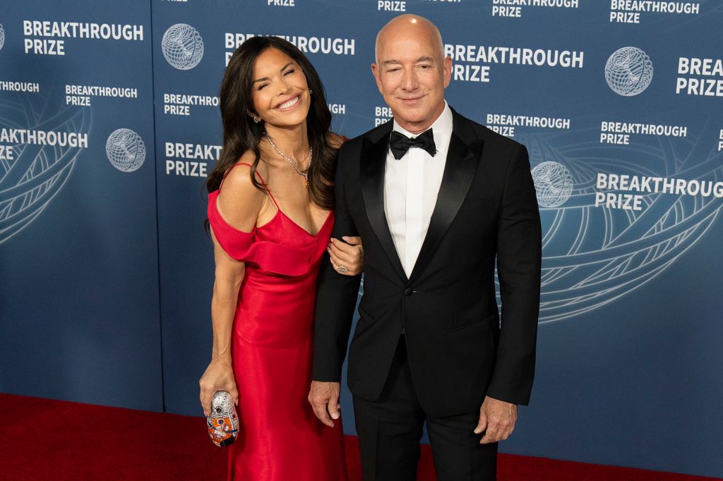 Lauren Sanchez smiling in a red dress holding the arm of Jeff Bezos who is wearing a suit 