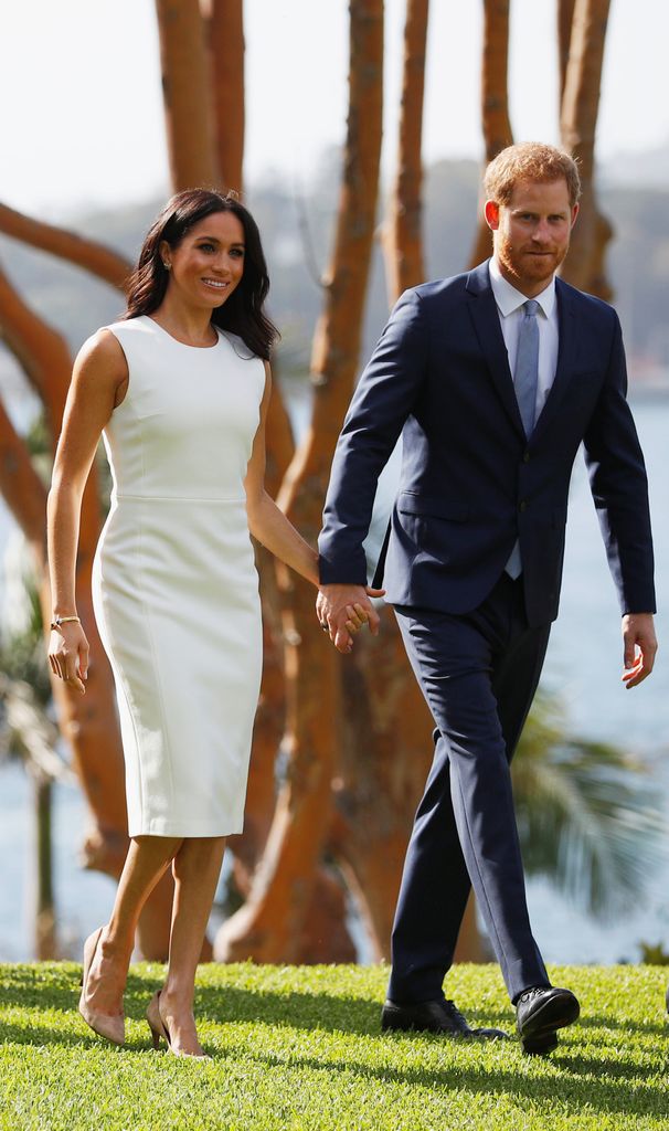 Meghan Markle in a white dress holding hands with Prince Harry