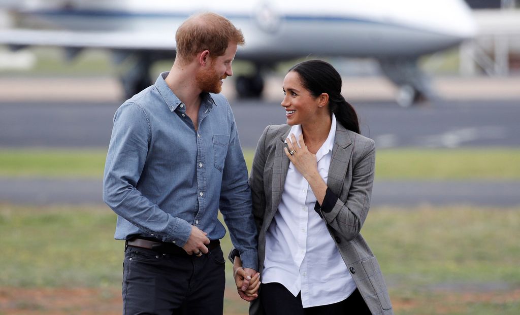 Prince Harry talking to Meghan Markle as they walk outside at an airport