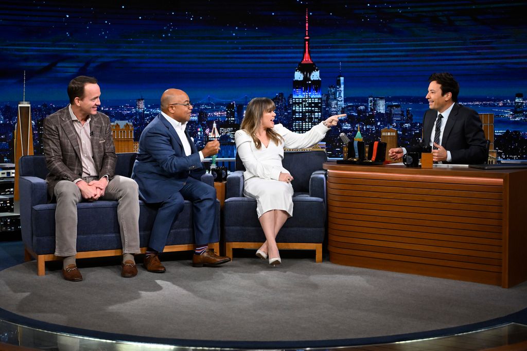 THE TONIGHT SHOW STARRING JIMMY FALLON -- Episode 1938 -- Pictured: Peyton Manning, Mike Tirico, and Kelly Clarkson share a special announcement during their interview with host Jimmy Fallon on Tuesday, March 12, 2024