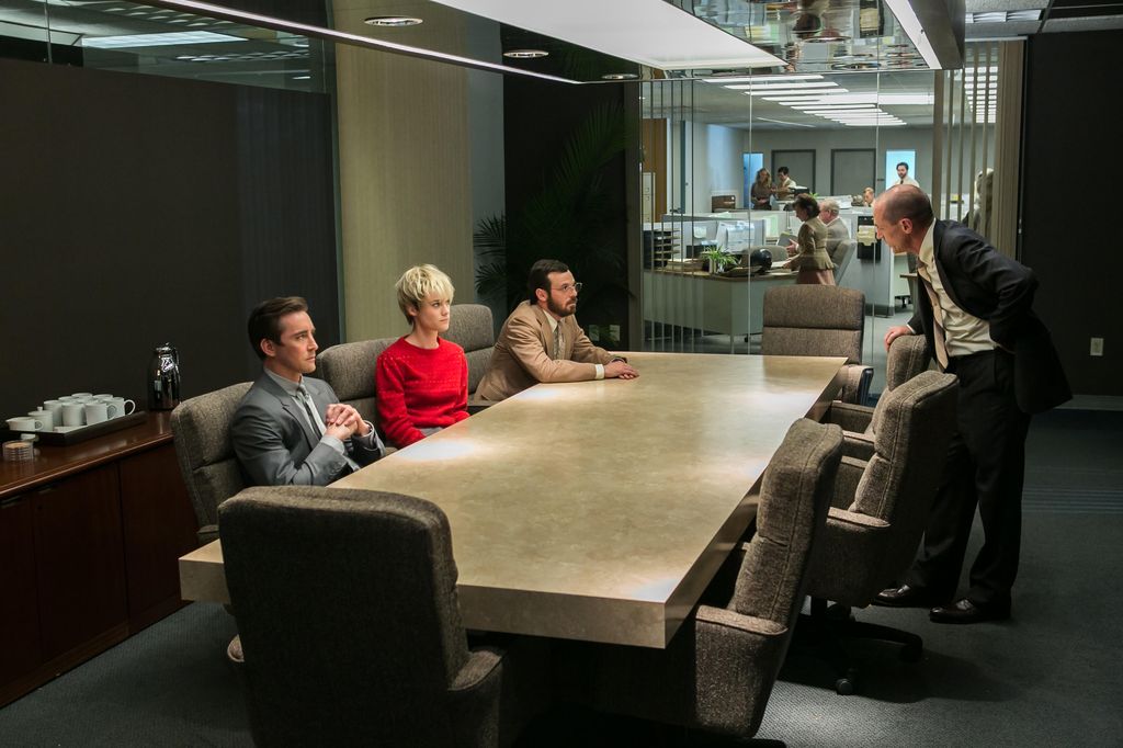 three people sitting at desk opposite standing man