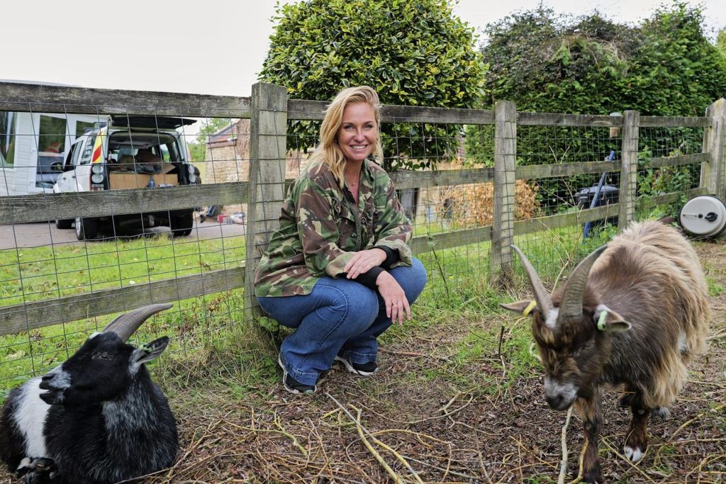 A woman crouches by two goats
