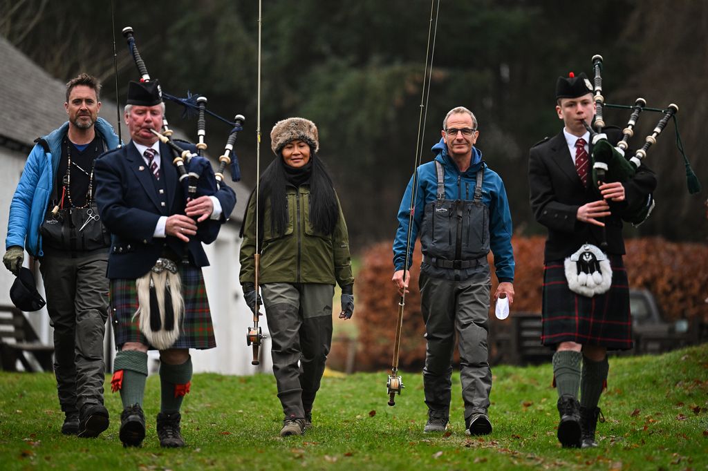 three people walking with fishing rods alongside two pipers