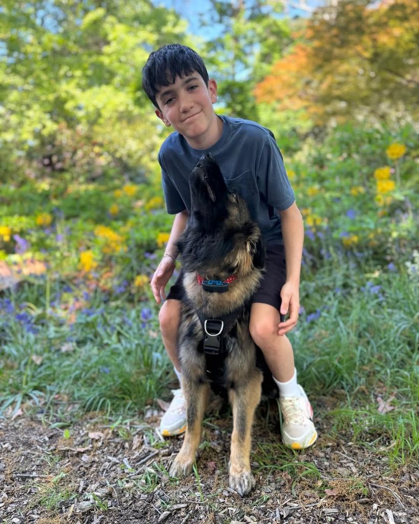 Eric Cowell smiling for camera with his dog, Pebbles, sitting between his feet while walking through woods