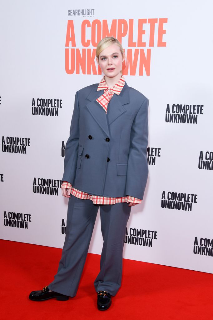 Elle Fanning on red carpet in grey suit and striped shirt