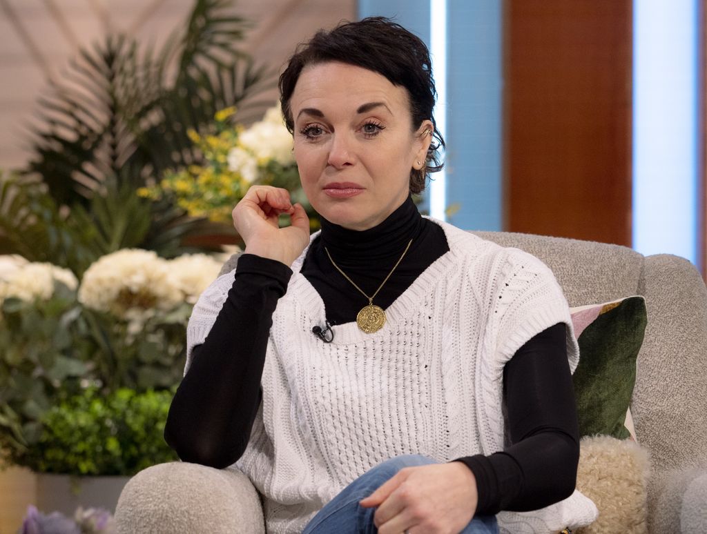 Amanda Abbington looking sad in a white cardigan and black turtleneck