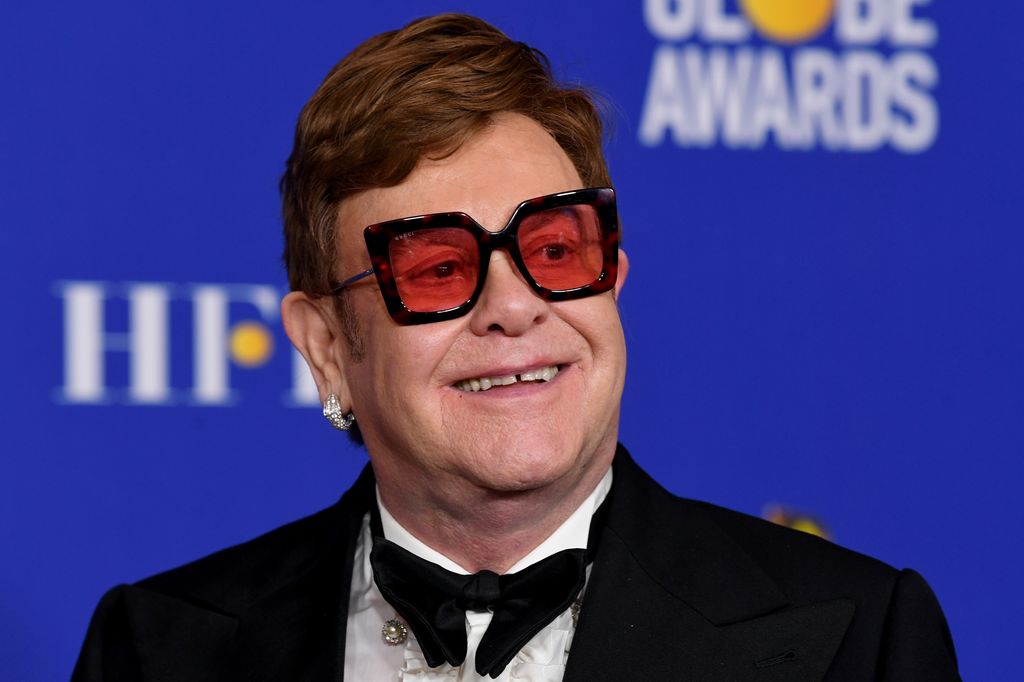 Sir Elton John wearing red-tinted glasses and a tuxedo while walking red carpet at golden globe awards