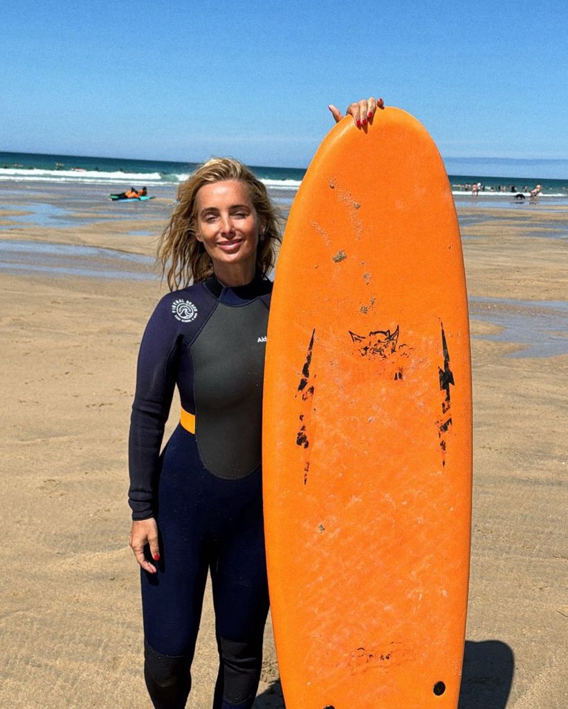 woman standing in wetsuit with surfboard