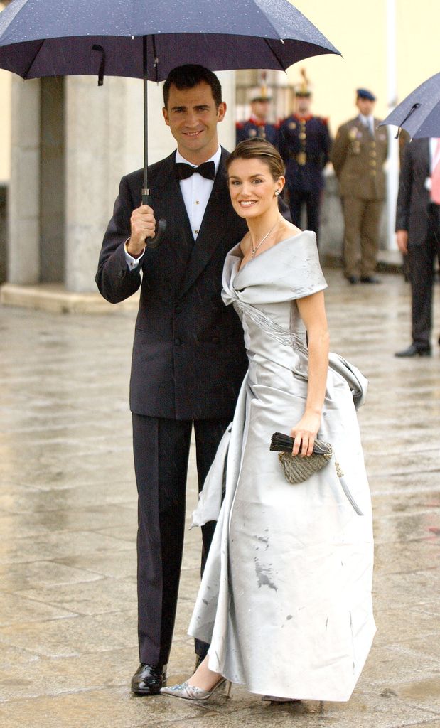 Queen Letizia in an off-the-shoulder silver dress under an umbrella with her husband