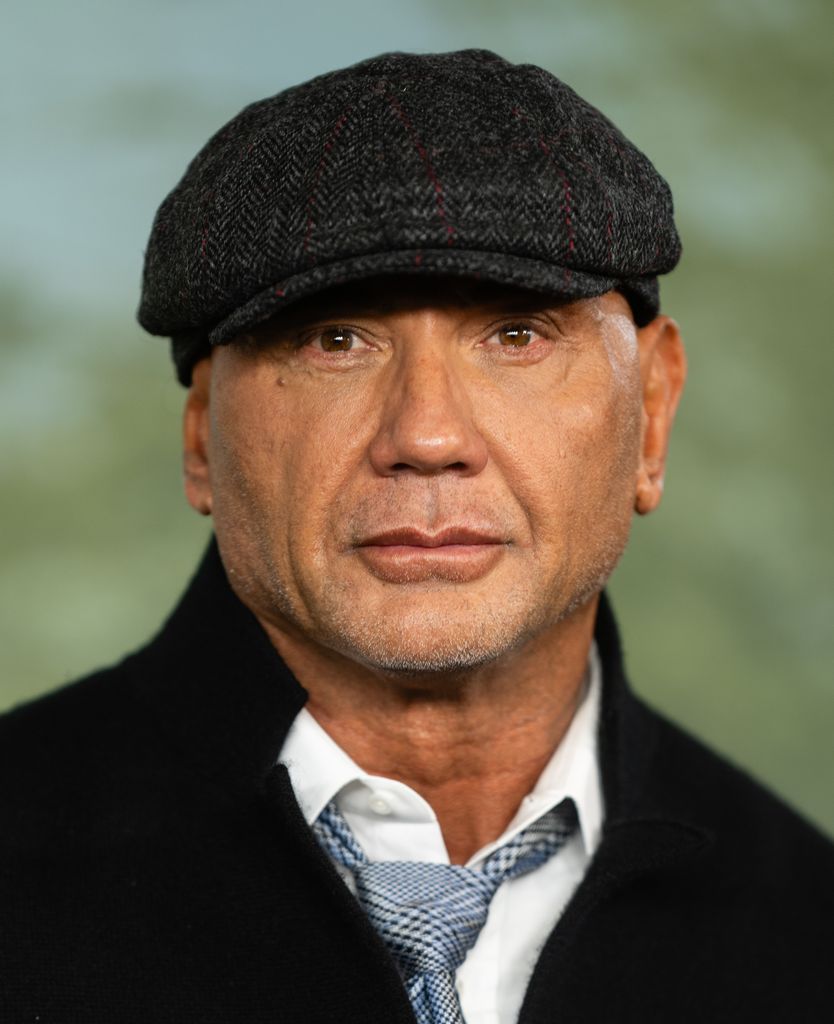 Dave Bautista porte une chemise, une veste noire et une casquette plate et regarde droit vers l'objectif de la caméra.
