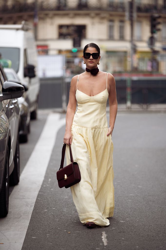 PARIS, FRANCE - FEBRUARY 28: Gili Biegun wears long yellow maxi dress, burgundy bag, matching burgundy neck accessory rose or flower and sunglasses  during the Womenswear Fall/Winter 2024/2025 as part of  Paris Fashion Week on February 28, 2024 in Paris, France. (Photo by Raimonda Kulikauskiene/Getty Images)