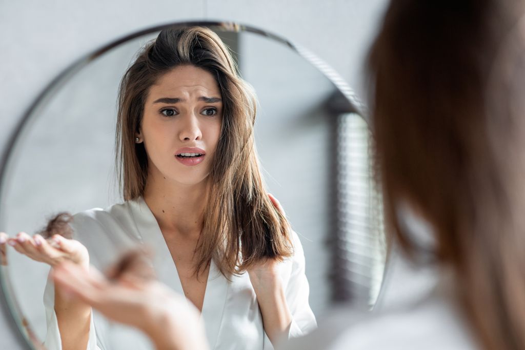 Portrait of stressed young woman with bunch of fallen hair in hand