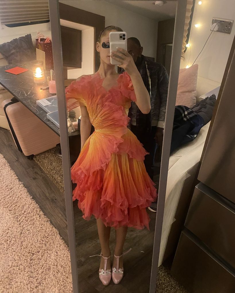 A BTS snap of Ariana trying on one of Glinda's amazing dresses in bright orange and yellow with big ruffles