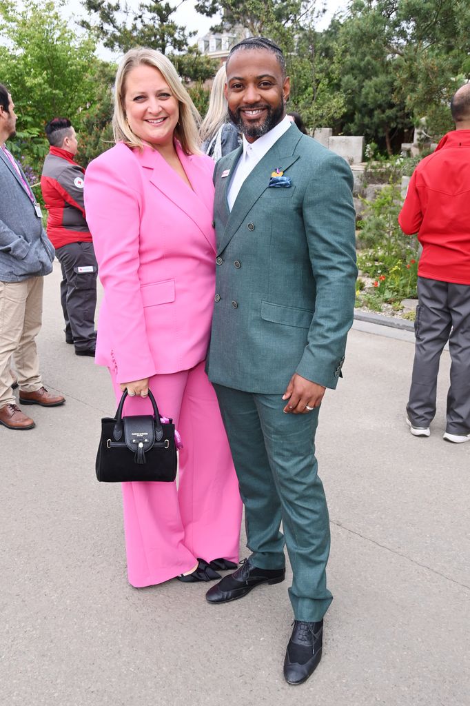 Chloe Gill in a pink suit and JB Gill in a green double-breasted suit pose arm in arm at the Chelsea Flower Show.