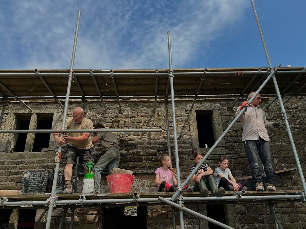 landscape shot of scaffolding outside farmhouse with construction workers working on renovation