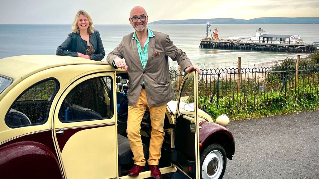 David Harper and a woman in front of a pier in an old car