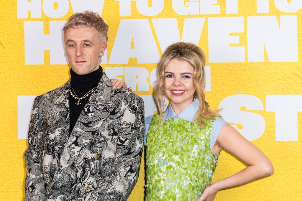 Denis Sulta portant un costume à motifs noir et blanc et Saoirse-Monica Jackson avec un bras sur l'épaule portant une robe à paillettes vertes scintillantes avec un col bleu