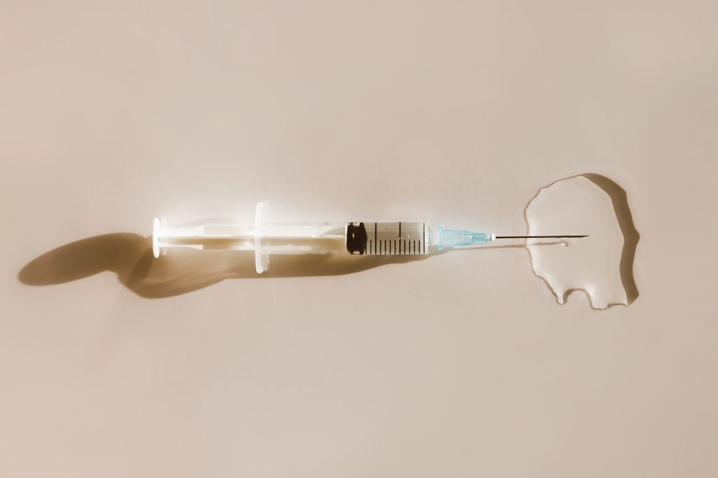 Top view of sterile syringe placed in puddle of transparent liquid drug on beige background