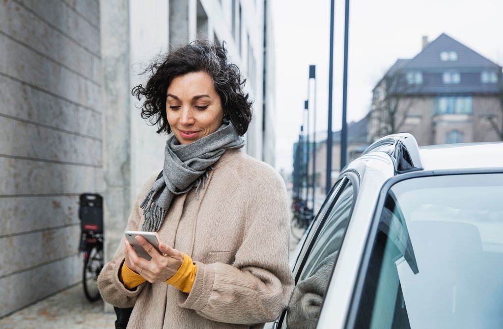 Woman texting with cellphone standing next to car