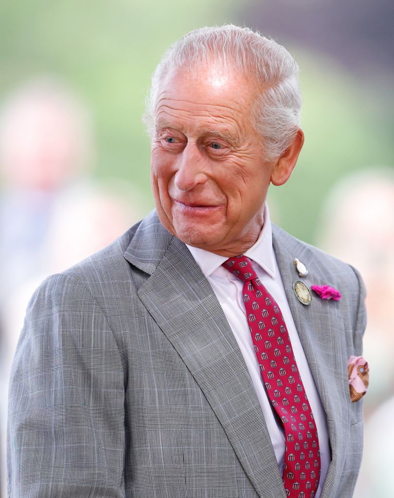 King Charles smiling over shoulder in grey suit