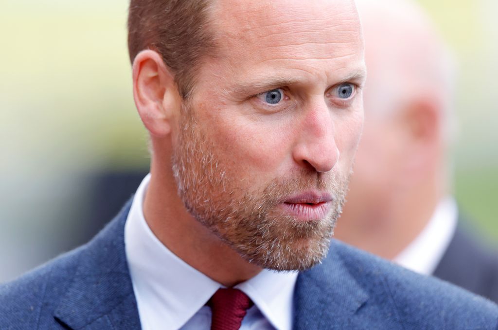 Prince William looking shocked and pursing his lips in a blue suit