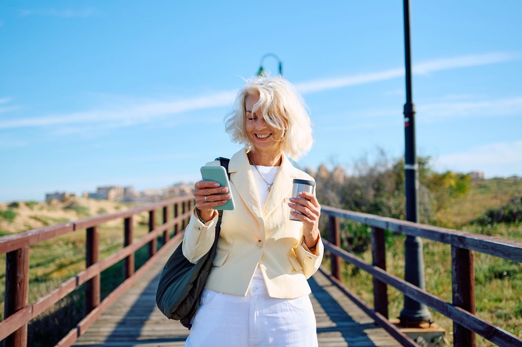 older woman looking at mobile phone and drinking coffee.