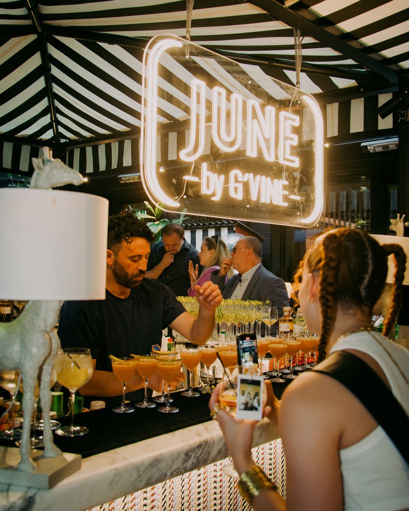 Bartender behind a bar with a row of cocktails under luminous sign