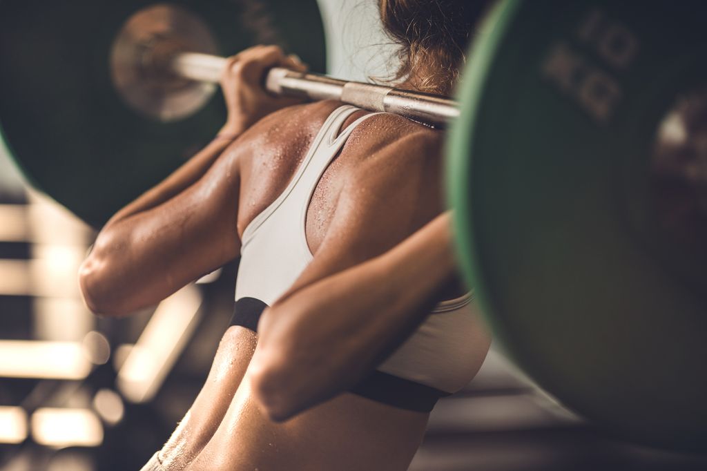 Unrecognizable sweaty woman doing back exercises with barbell.