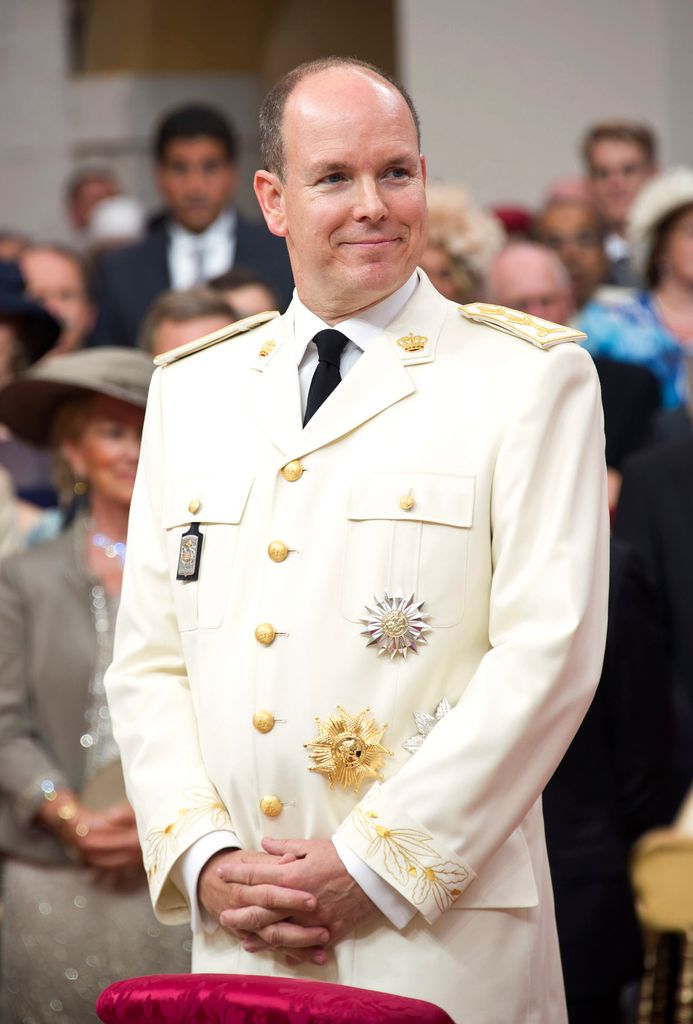 Prince Albert II of Monaco smiling in a white suit at the altar