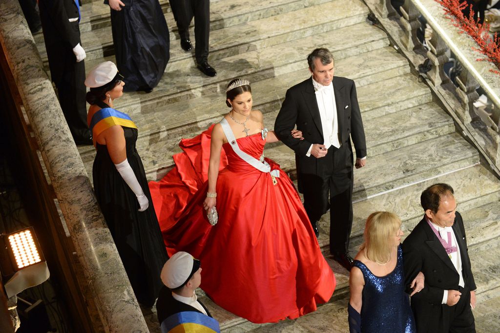Eric Betzig (R) and Swedish Crown Princess Victoria in red gown descend steps