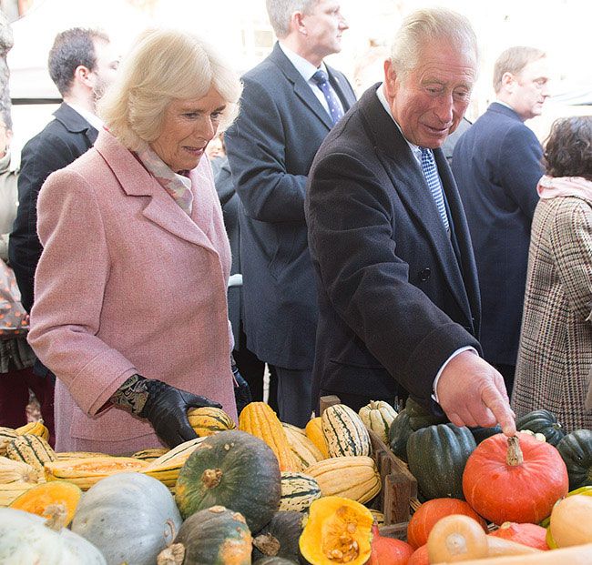charles points to a pumpkin at a squash stall and camilla watches