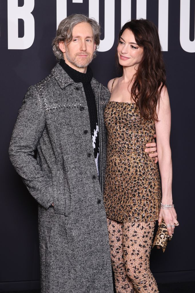 Anne Hathaway in a leopard dress looking at Adam Shulman wearing a grey long coat