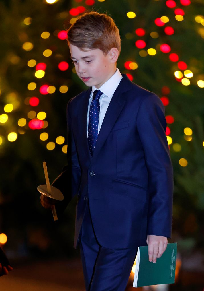 Prince George in a blue suit holding a candle
