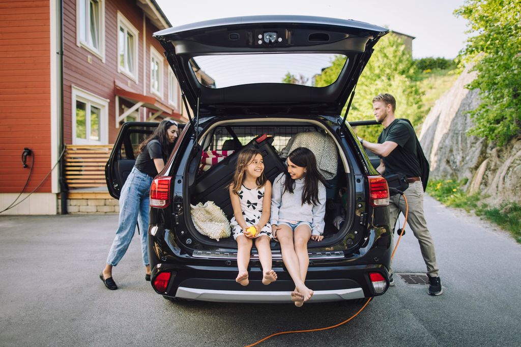 Father and mother loading car with happy daughters sitting in trunk