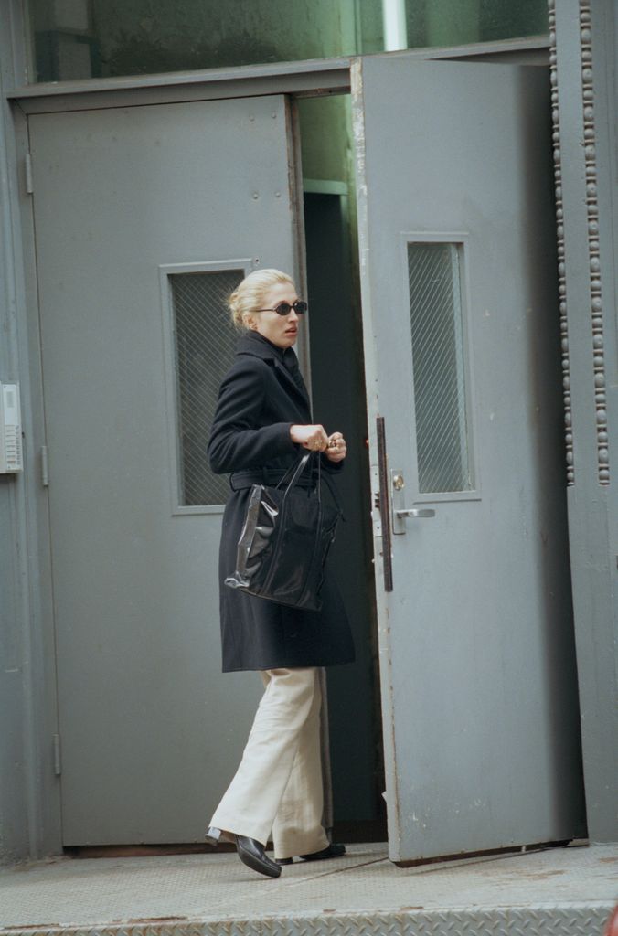 Carolyn Bessette-Kennedy arriving home in New York  wearing a black coat, round sunglasses and cream trousers