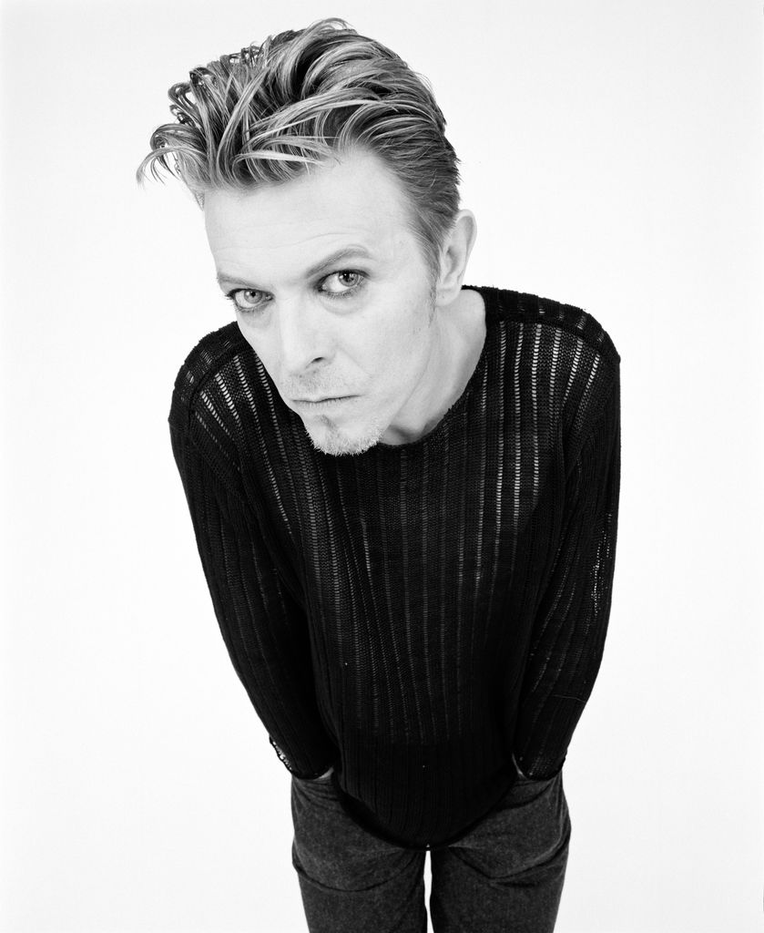 Black-and-white image of Dabid Bowie in a translucent black shirt and jeans
