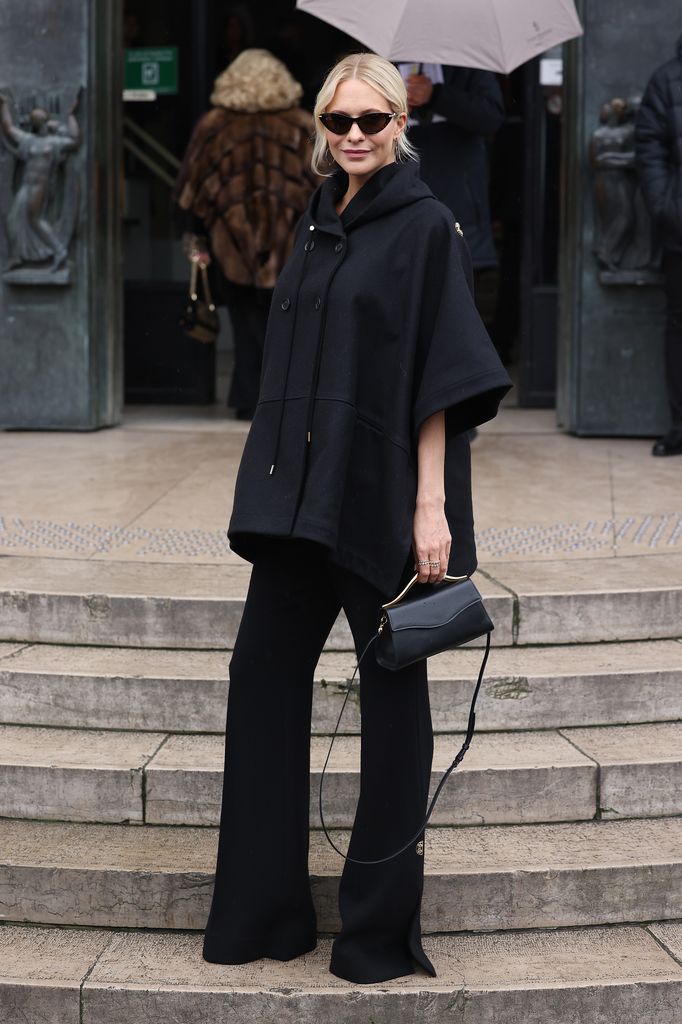 Poppy Delevingne wore an all-black look with a voluminous wool hoodie cape, sleek tailored trousers, and dark cat-eye sunglasses, delivering effortless Parisian chic.