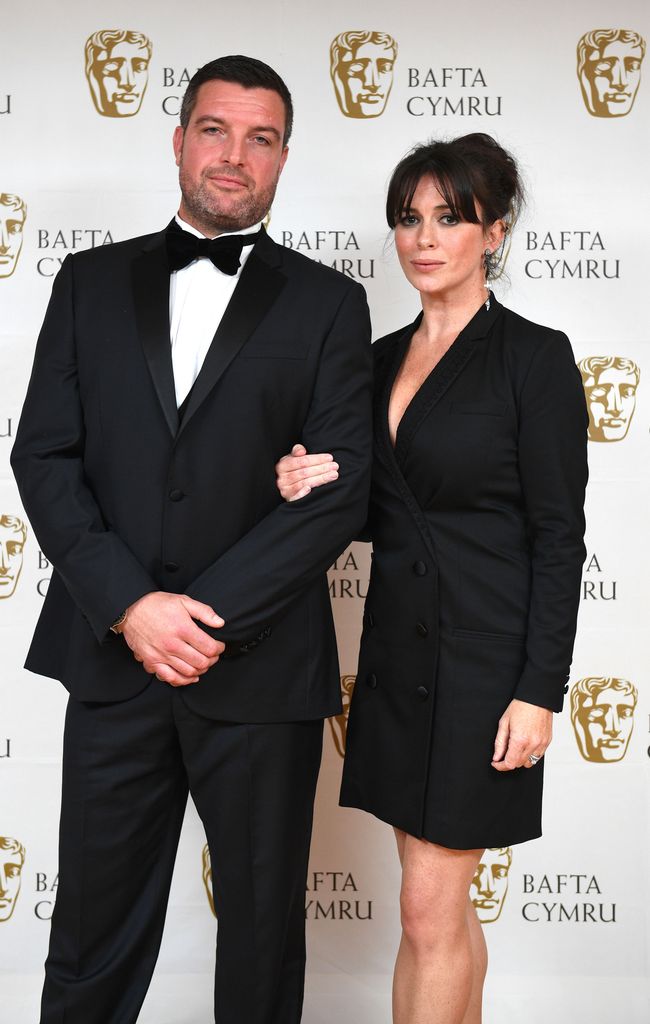 man and woman posing on red carpet in black tie dress