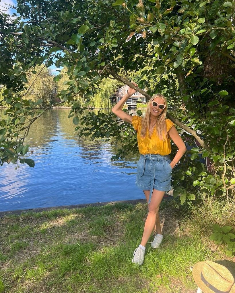 Tess Daly in denim shorts standing in front of lake