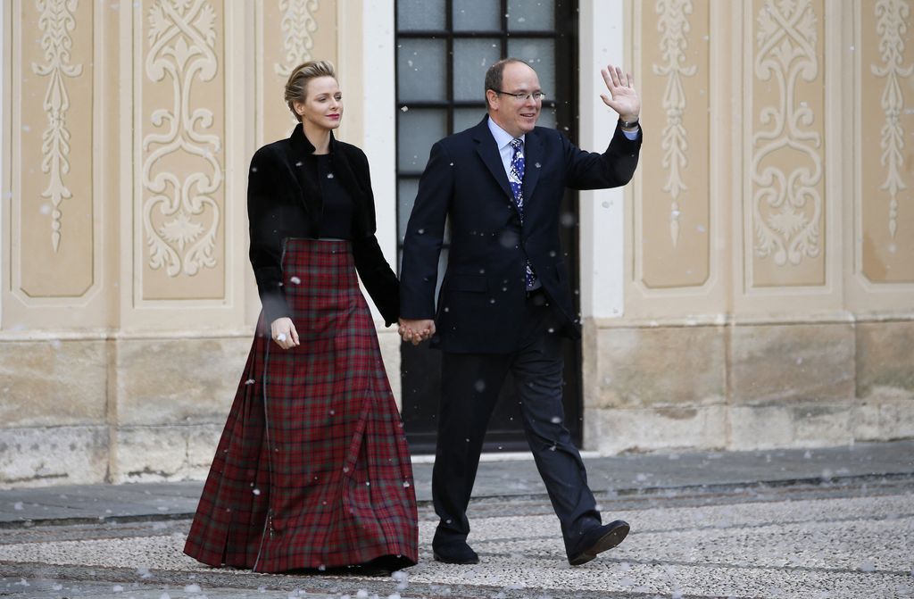 Prince Albert II of Monaco waves flanked by his wife Charlene wearing floor length tartan skirt 