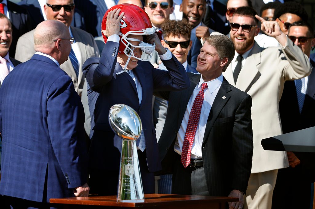 Le président américain Joe Biden enfile un casque que lui ont offert l'entraîneur-chef des champions du Super Bowl de la NFL, Andy Reid (à gauche), et le PDG Clark Hunt des Chiefs de Kansas City, sur la pelouse sud de la Maison Blanche.