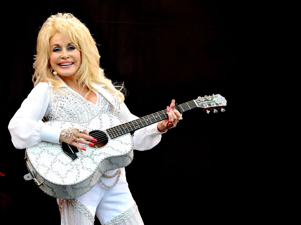 Dolly Parton in a sparkling white suit holding a guitar 