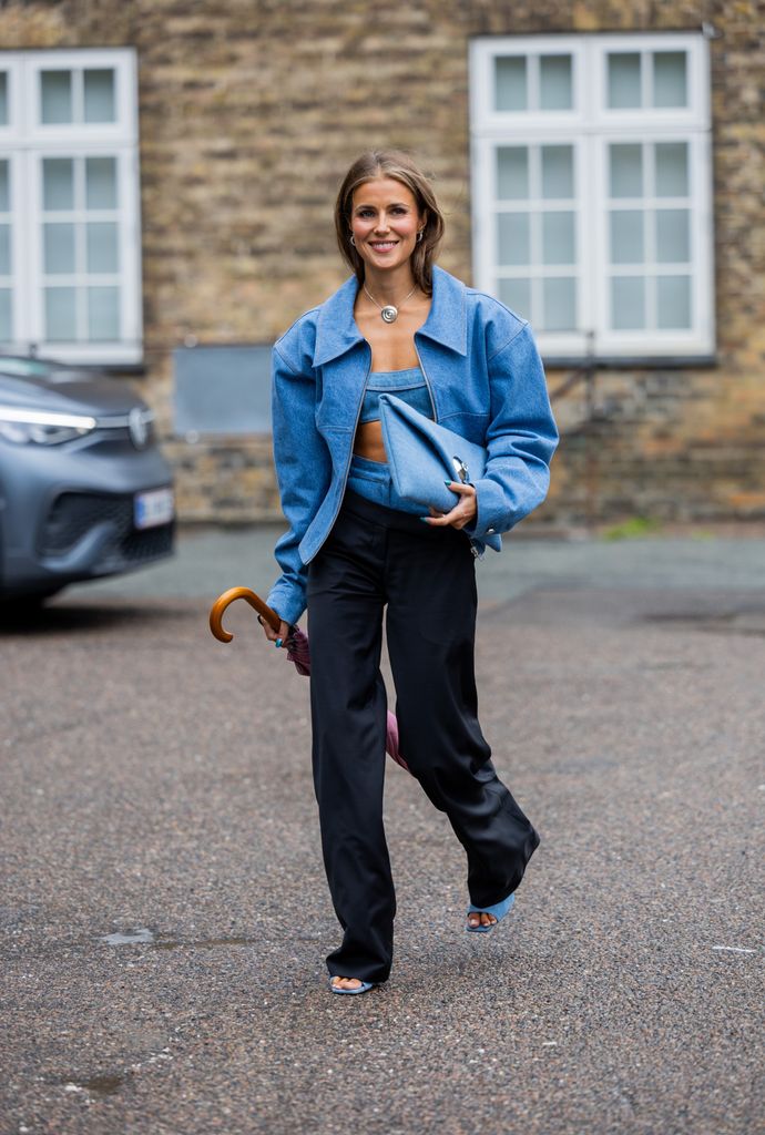 Nina Sandbech wears oversized denim jacket, clutch, mixed denim black pants, heels, cropped top outside 7 Days Active during the Copenhagen Fashion Week Spring/Summer 2024