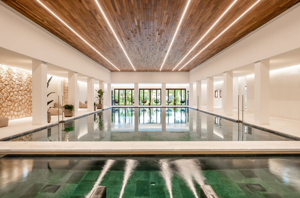 indoor spa pool at Kimpton Aysla Mallorca, highlighted by striking wooden ceiling beams, modern lighting, and a tranquil setting with views of the surrounding gardens.