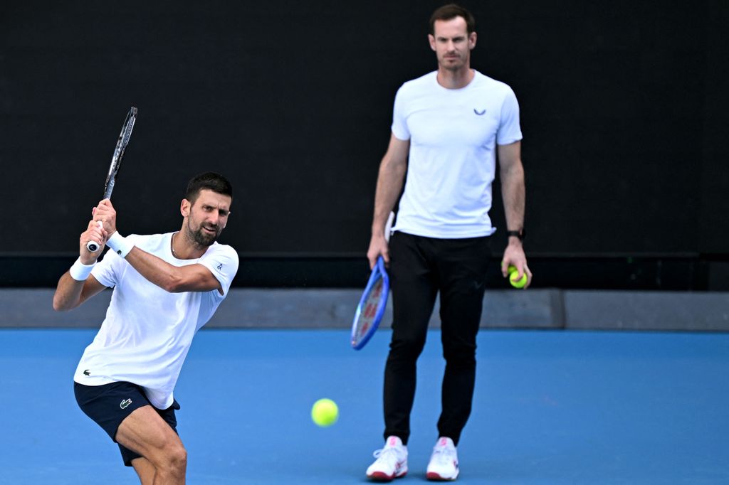 Novak Djokovic hits a return as coach Andy Murray looks on