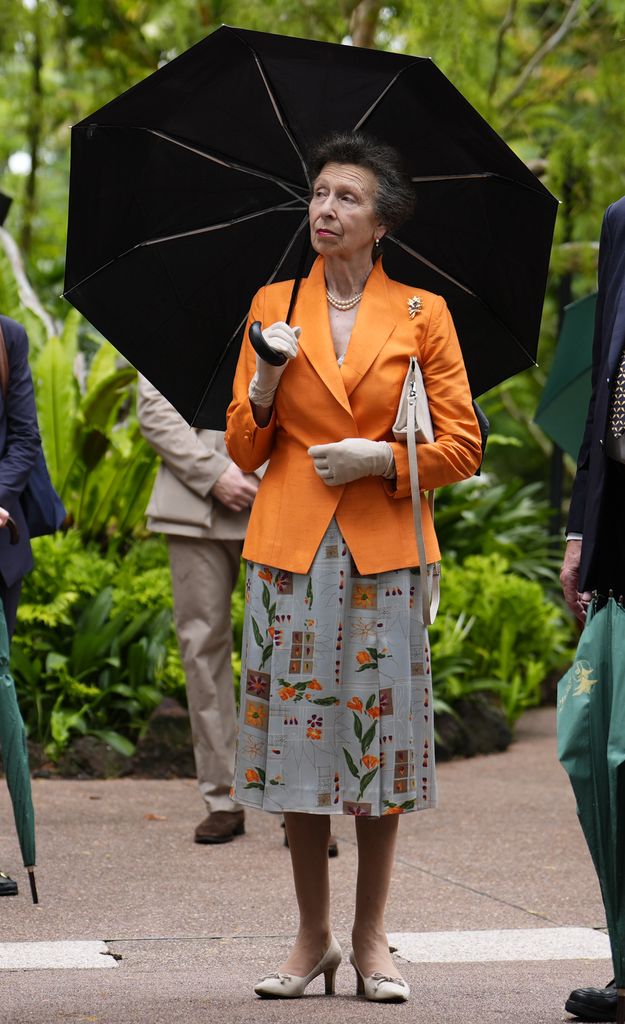 The Princess Royal holding umbrella in orange blazer and printed dress