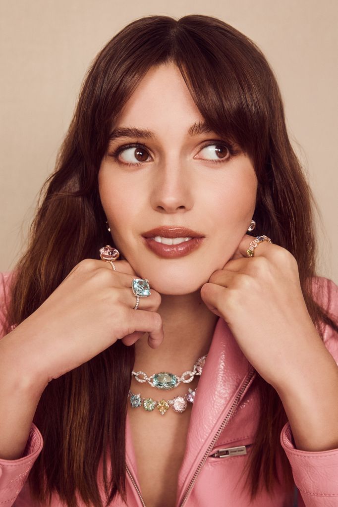 In a pastel pink Miu Miu leather jacket, Ruby Sear highlights a multi-hued Bucherer necklace and oversized gemstone rings. Her soft smile complements the colourful, luxurious jewellery.